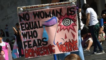 A demonstrator's sign reads, "No woman is equal who fears domestic violence."