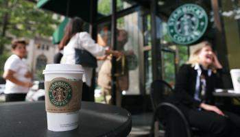 Patrons enter a Starbucks as a cup from the store sits on a table.