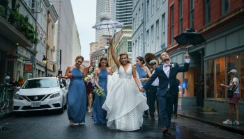 A New Orleans wedding group parades down a street, umbrellas in hand.