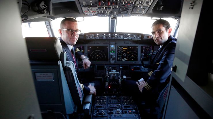 Two pilots pose in an airplane cockpit.