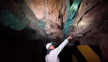 A man points to blue-green mineral seams in a cave.