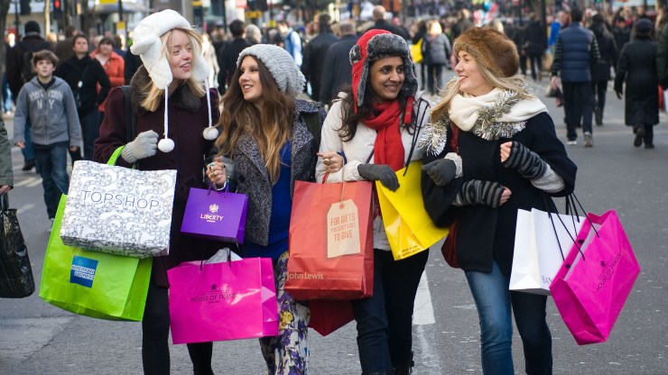 Four women walk arm-in-arm down a crowded street holding tons of shopping bags.
