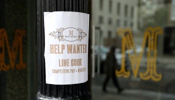 A "Help Wanted" sign posted outside of a restaurant.