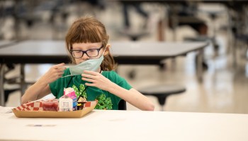 A child takes off their mask to eat a school lunch.
