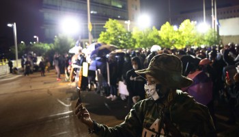 A woman wearing a George Floyd mask records a video during a standoff between demonstrators and police officers in front of the public safety building after a peaceful march for Daniel Prude on September 7, 2020 in Rochester, New York.
