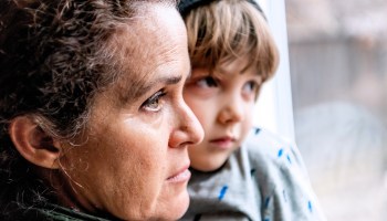A mother and son look out a window. More families will be eligible for the newly expanded child tax credit.