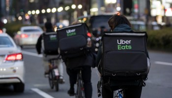 Uber Eats delivery workers ride bicycles wearing food bags on their backs.