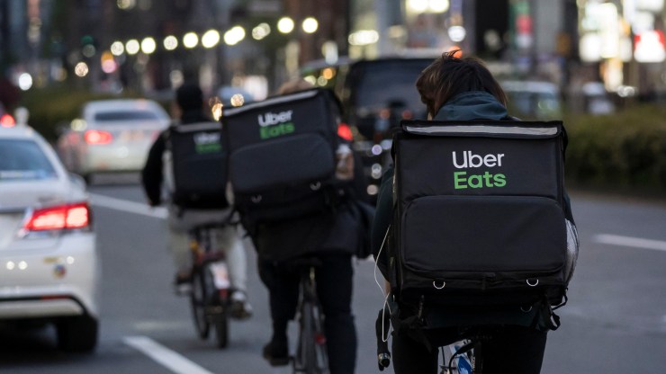 Uber Eats delivery workers ride bicycles wearing food bags on their backs.