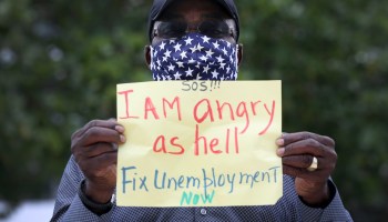 A protester holds a sign reading "SOS, I am angry as hell, fix unemployment now"