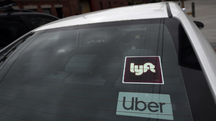 The rear windshield of a car displays stickers with the Lyft and Uber logos.