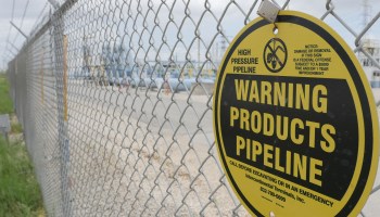 A yellow warning sign hangs on a barbed wire fence at the Colonial Pipeline Houston Station in Texas.