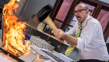 A stock photo of a frustrated businessman hitting laptop on fire with hammer.