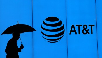 A person holding an umbrella walks in front of an AT&T sign.