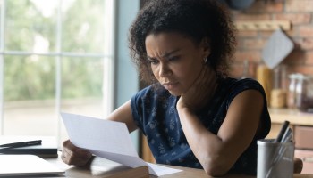 Frustrated young African American woman reading letter with bad news.
