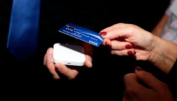 A hand taps a credit card to a pay in a contactless manner.
