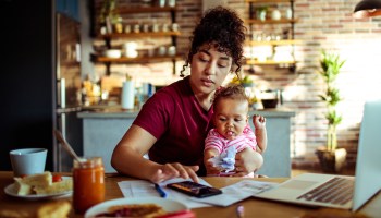 A busy mother using her phone and holding her child while having breakfast and dealing with paperwork.