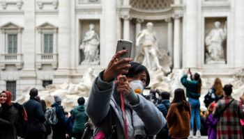A tourist wearing a respiratory mask takes a selfie at the Trevi fountain.