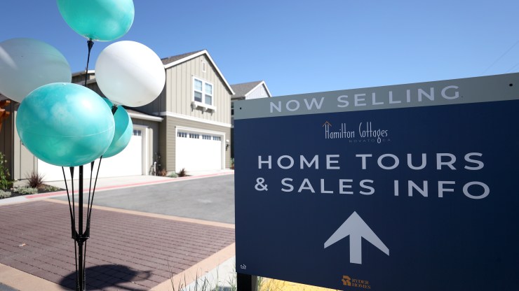 A sign advertises home tours and sales at a housing development.