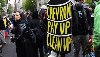 Protesters hold a sign saying "Chevron, Pay Up, Clean Up."