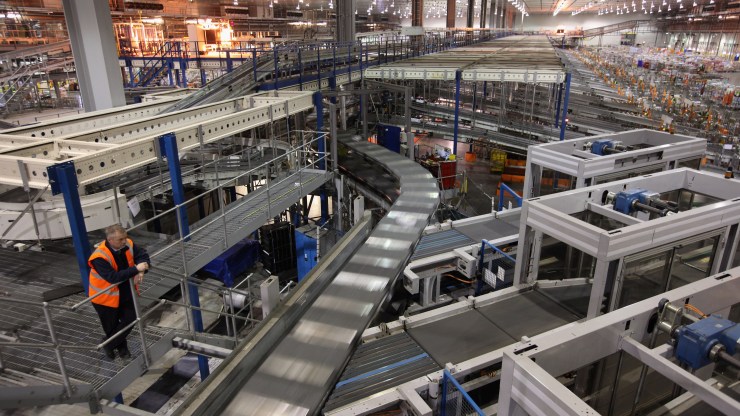 A man looks out over a railing at a warehouse full of automated sorting machines.