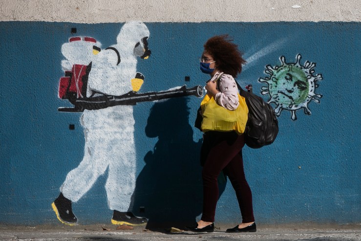A woman wearing a mask walks past a wall with a graffiti depicting a cleaner in protective gear spraying viruses with the face of President Jair Bolsonaro in Estacio neighborhood amidst the coronavirus (COVID-19) pandemic on June 8, 2020 in Rio de Janeiro, Brazil.