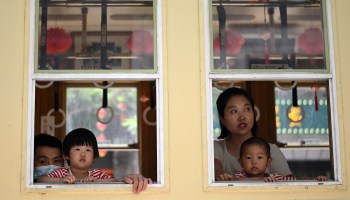 Children peek out from a window with their parents along Qianmen Street, a popular touris, and shopping area, on International Children's Day in Beijing on June 1, 2021.