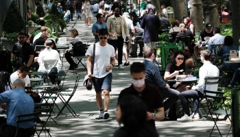 Dozens of people, some masked and some not, walk, eat or chat in New York City's Bryant Park.