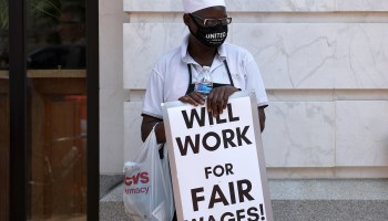 A worker at a demonstration with a sign that reads, "Will work for fair wages!"