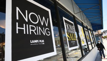 A pedestrian walks by a "now hiring" sign outside of a Lamps Plus store on June 03, 2021 in San Francisco, California.