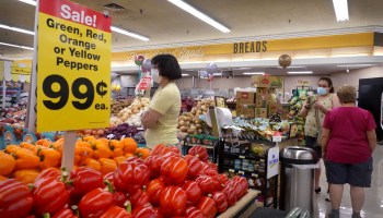 Red bell peppers are on sale in a grocery store, where masked customers shop.