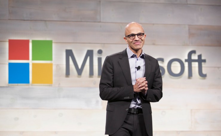 CEO and Chairman of Microsoft Satya Nadella stands in front of a wall with the Microsoft logo on it during a shareholders meeting.