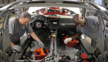 Two men do mechanical work on the interior of a car's body.