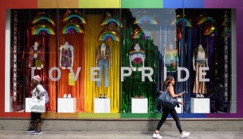 Two women walk past a storefront decorated in rainbows, with rainbow-color clothing.