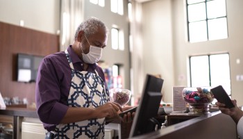 An older man working at a cash register. The problem of age discrimination, which hurts older workers and reduces GDP, may have worsened during the COVID-19 pandemic.