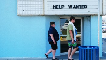 Two people walk past a sign reading "Help Wanted."