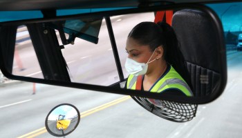 A shot of a bus rearview mirror with a female driver in view.