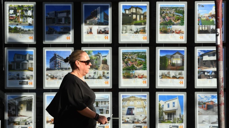 A woman walks past a window full of real estate listings.