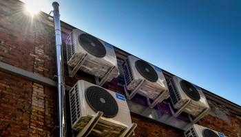 Air conditioning units on the side of a building underneath a blazing sun.
