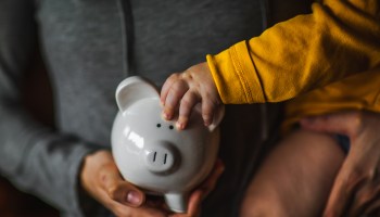 An adult and child hold a piggy bank.