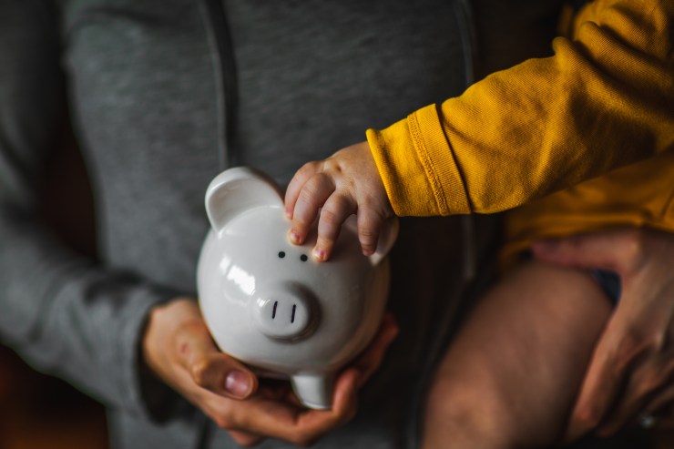 An adult and child hold a piggy bank.