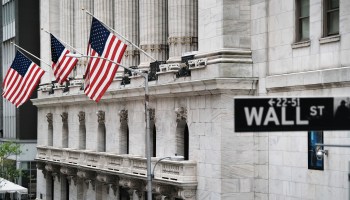The New York Stock Exchange is pictured behind the Wall Street sign.