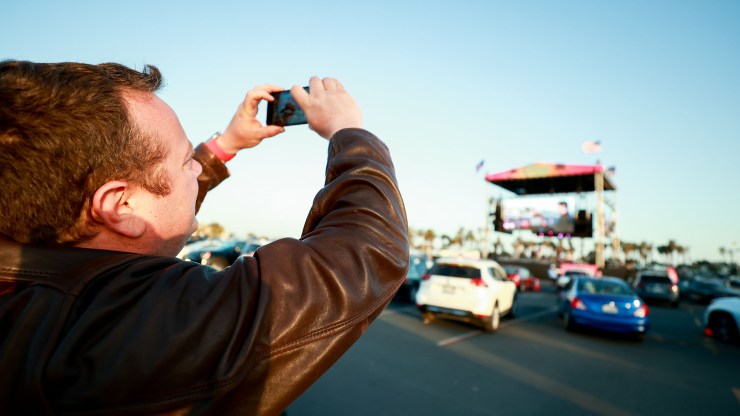 A man holds up a phone to record a band performing onstage.