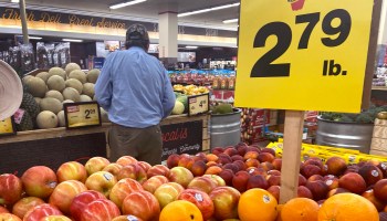 A man looks at fresh produce behind a sign that reads $2.79 a pound for oranges.