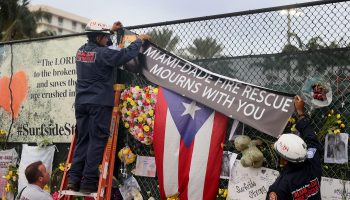 Search and rescue personnel place a banner at the memorial for the victims of the collapsed Champlain Towers South condominium in Surfside, Florida.