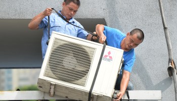 Workers install an air conditioning unit in a food stall in Shanghai in 2013. In a new book called "After Cooling," writer Eric Dean Wilson wrestles with the societal costs of individual air conditioning.