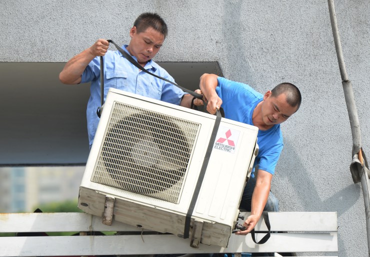 Workers install an air conditioning unit in a food stall in Shanghai in 2013. In a new book called "After Cooling," writer Eric Dean Wilson wrestles with the societal costs of individual air conditioning.