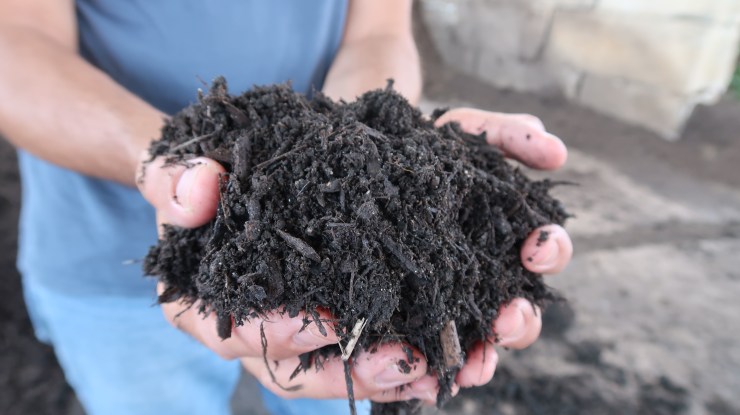 Chris Peot, director of resource recovery at DC Water, holds a mound of dark, brown Bloom fertilizer in his hands. 