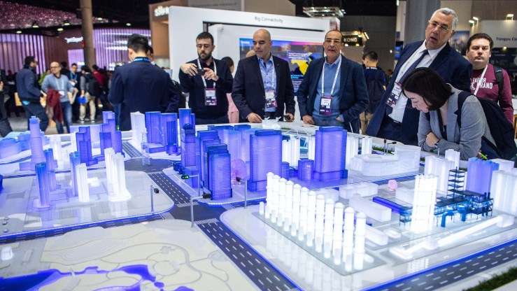 Bystanders view a 5G blue Chinese model city showing smaller blue and white luminescent buildings.
