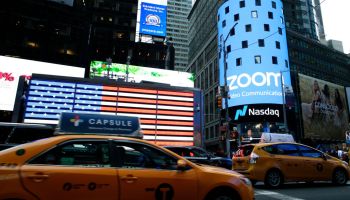 People pass by the Nasdaq building as the screen shows the logo of the video-conferencing software company Zoom after the opening bell ceremony on April 18, 2019 in New York City.