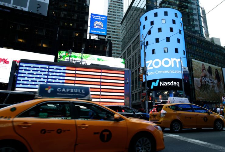 People pass by the Nasdaq building as the screen shows the logo of the video-conferencing software company Zoom after the opening bell ceremony on April 18, 2019 in New York City.